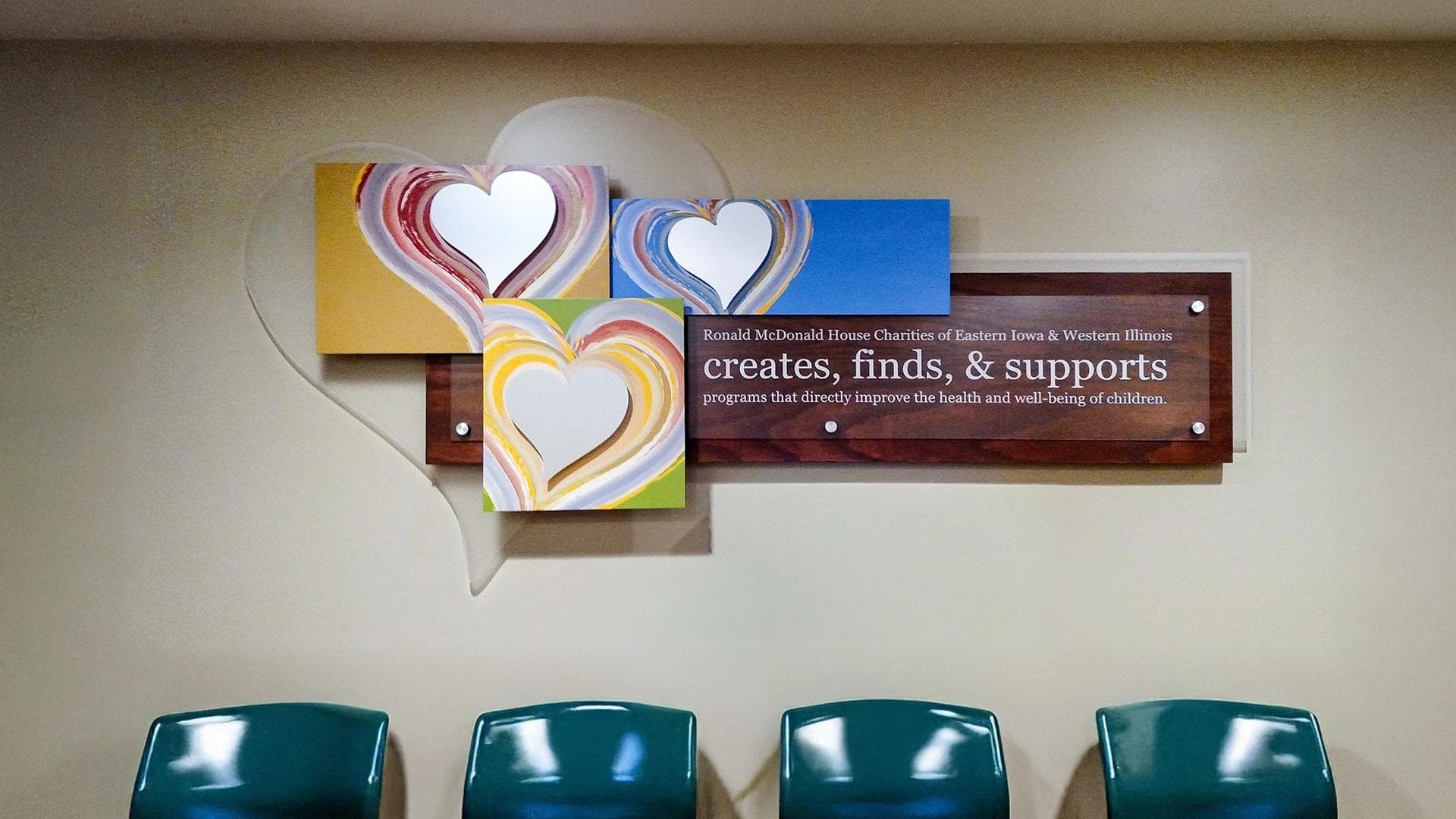 Ronald McDonald House Charities donor recognition plaque with colorful heart panels and mission statement mounted above seating area.