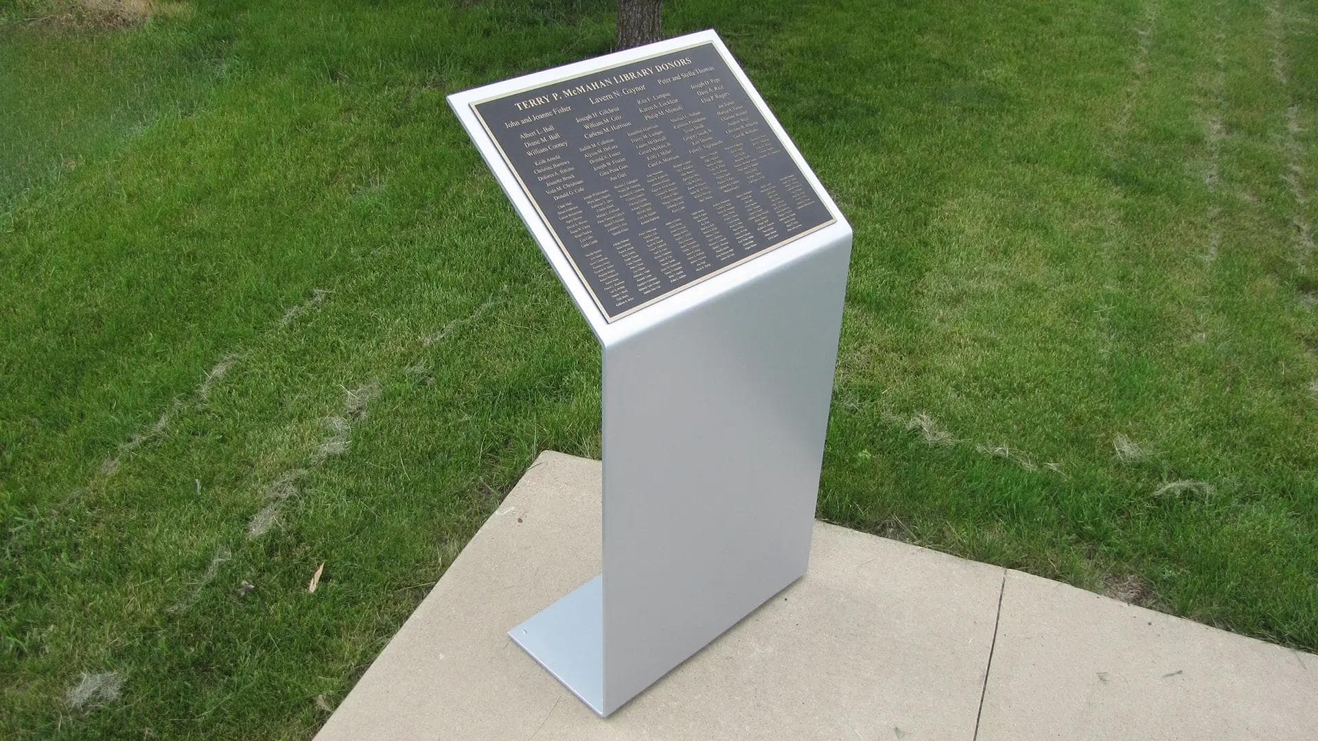 Hodges University outdoor donor recognition pedestal with bronze plaque listing library donors in a landscaped campus setting.