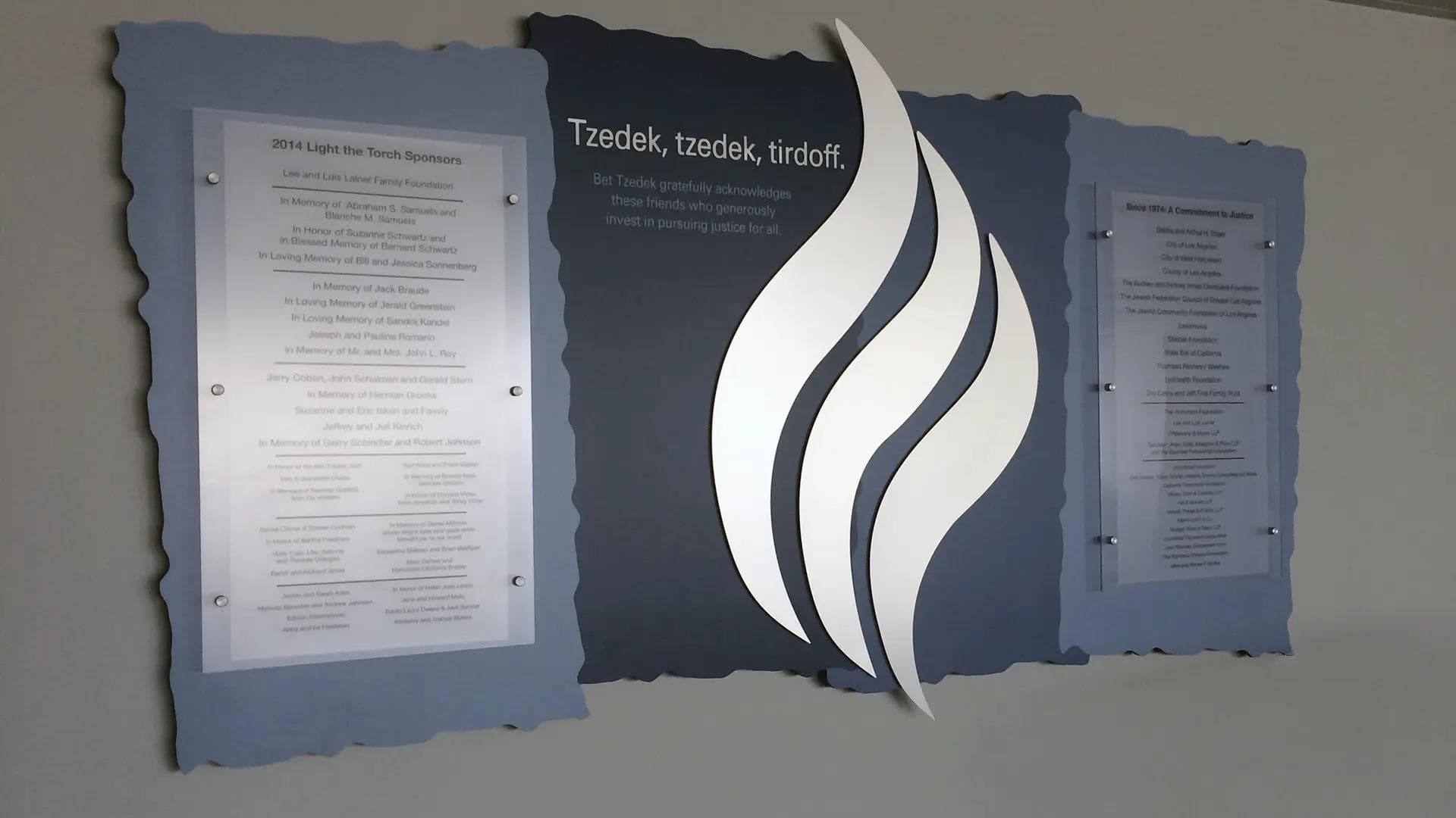 Jewish donor recognition wall featuring Bet Tzedek justice theme with layered panels, donor plaques, and a dimensional flame centerpiece.