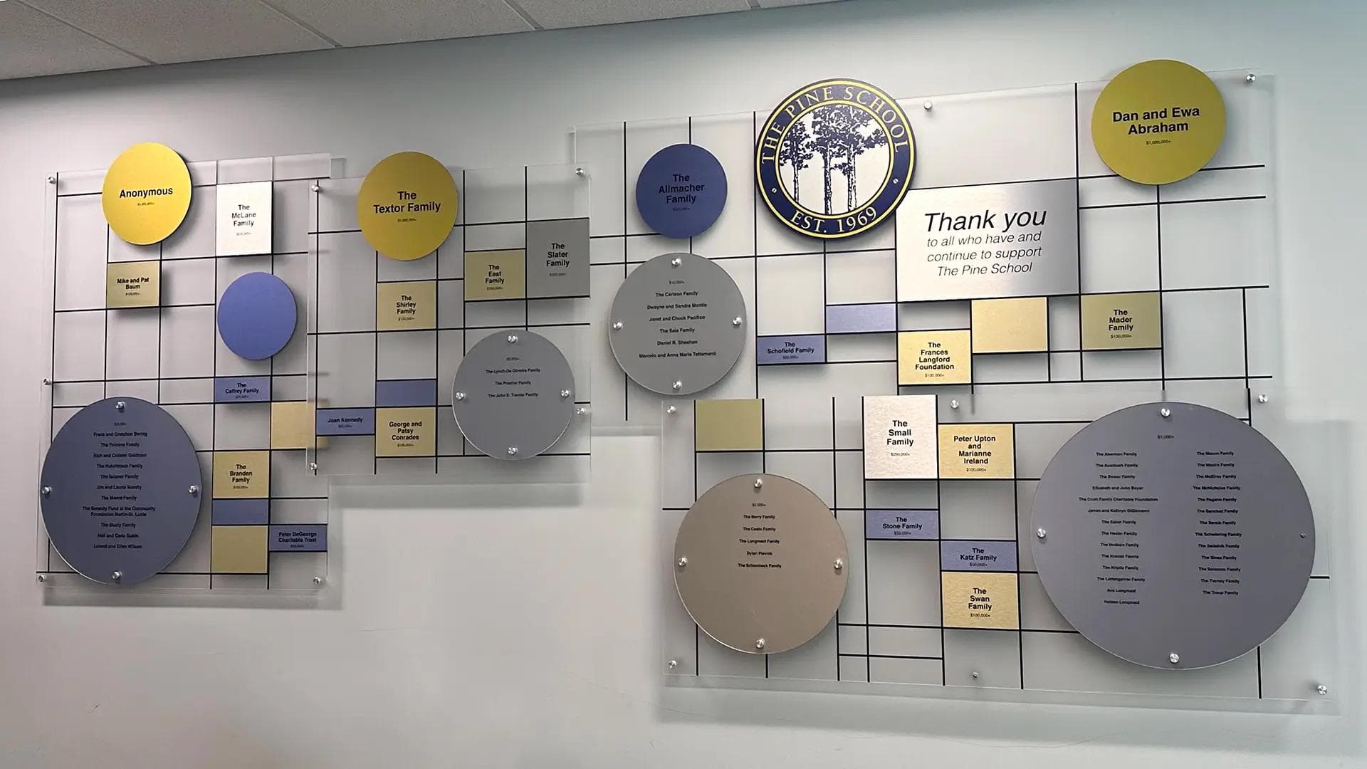 The Pine School donor recognition wall with individual naming tiles and circular plaques mounted on a clear grid acrylic wall.