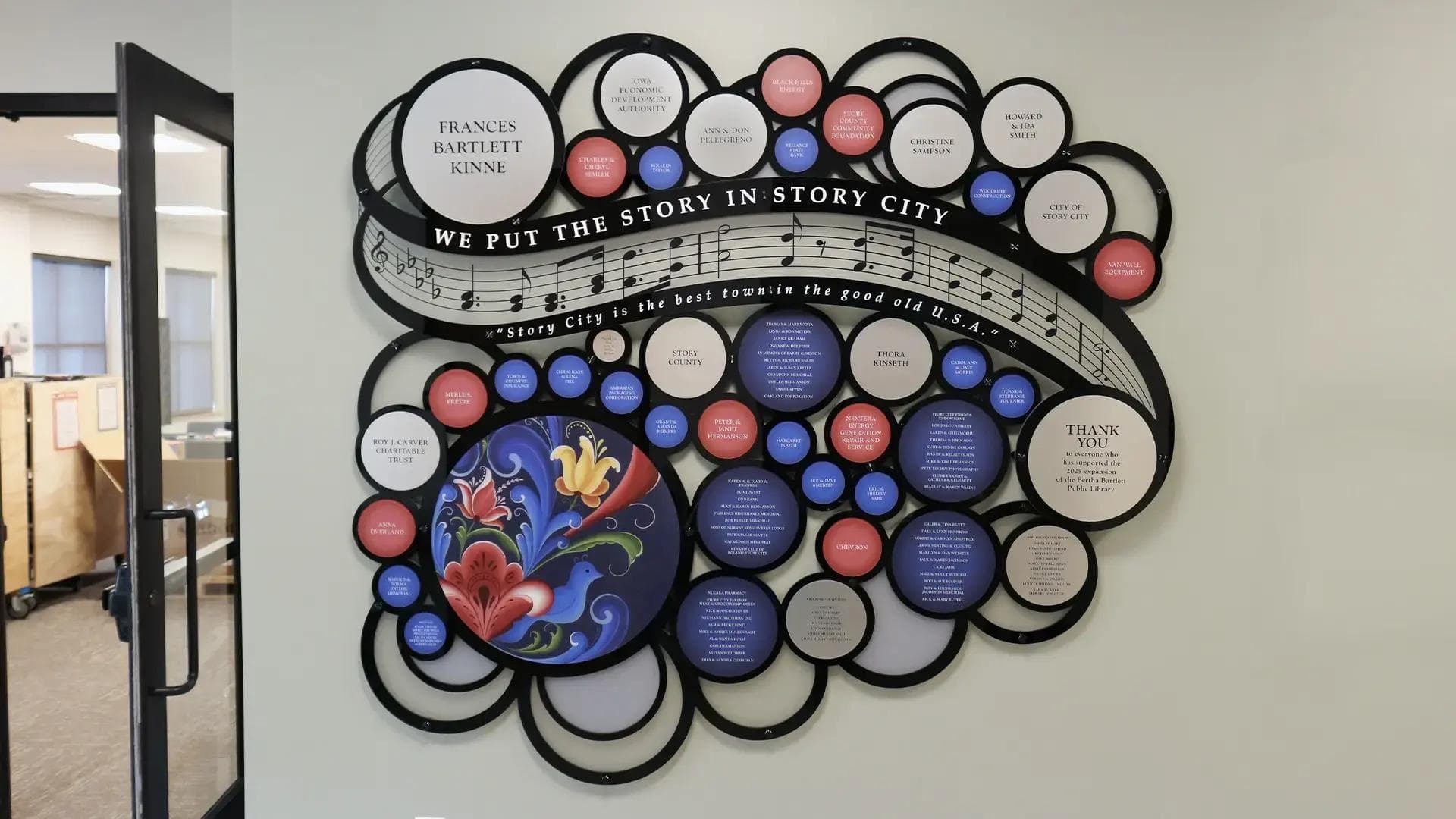 Story County Bertha Bartlett Public Library donor recognition wall featuring circular plaques and Scandinavian rosemaling artwork.