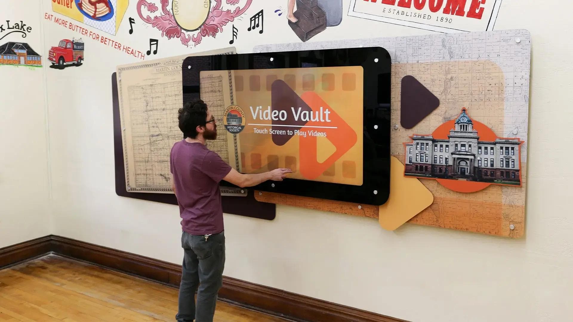 Interactive 65-inch touchscreen video wall with custom monitor surround playing local history videos in a history museum gallery.