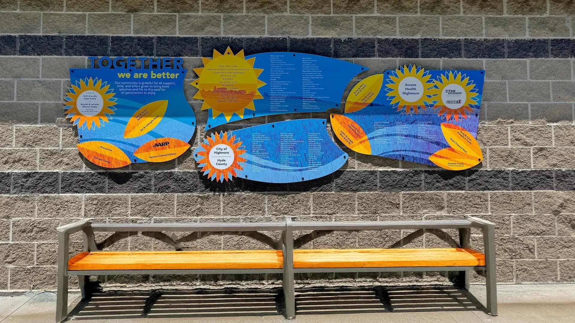 Outdoor donor recognition wall for the Highmore Community Pool project with colorful acrylic panels and sponsor names above a bench.
