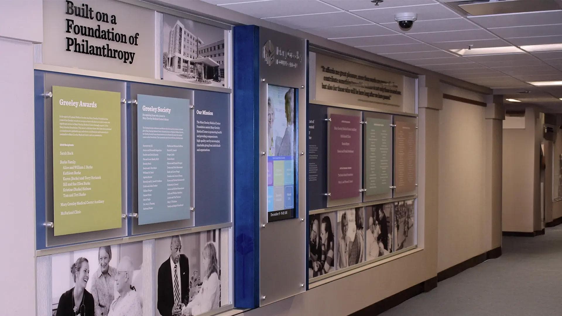 Healthcare donor recognition wall with colorful glass panels and an interactive digital display honoring philanthropy in a hospital corridor.