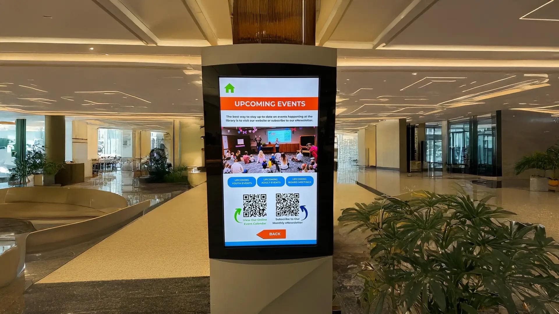 Public Library donor display and interactive digital kiosk showing upcoming events with QR codes in a modern lobby.