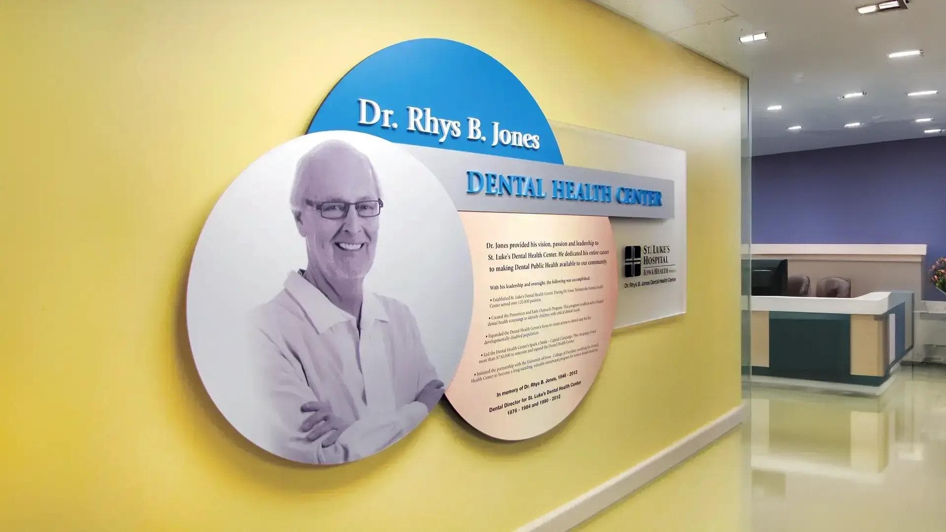 Donor recognition plaque sign with layered circular panels, portrait imagery, and dimensional lettering in a dental health center hallway.